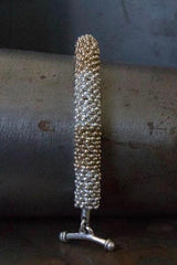 A chunky bracelet in silver and gold plated silver made from lots of daisy charms strung in a pleasing snake shape