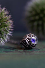 Close up of a special birthstone pendant for December – its centrepiece is a tactile textured ball with a glistening Tanzanite at the base.