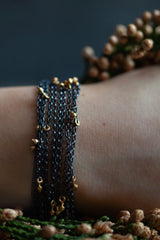 My Five Strand Trace and Pip Necklace worn like a bracelet comprises five delicate oxidised silver chains, decorated with miniature gold plated pips