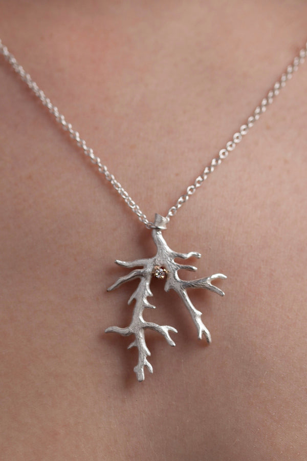 An unusual branch pendant, set with a Cubic Zirconia, April's birthstone, is shown on a model hanging from a delicate trace chain that can be worn at two lengths.
