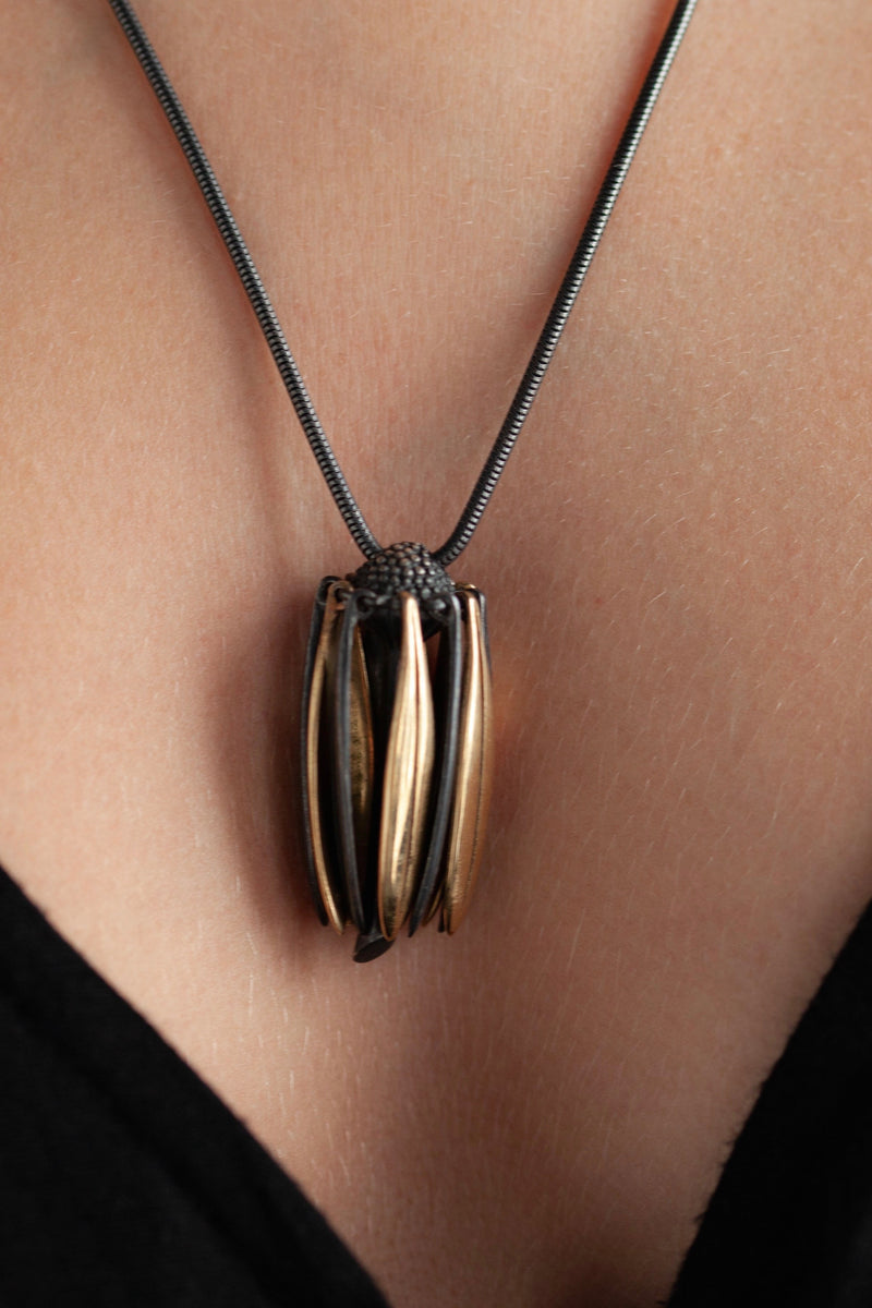 Close up of my Aster Pendant Necklace worn by a model  like a tassel with its bobbled head fringed with a series of long elegant flowing petals nestled in her decolletage