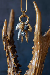 An elegant contemporary pendant necklace on a gold chain featuring nine charms in different metals inspired by seed pods