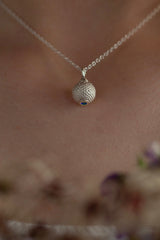 A birthstone pendant for November worn by a model – a tactile textured ball with a Swiss Blue Topaz