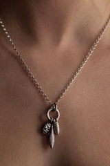Short pendant necklace worn by model with a cluster of 3 charms inspired by seed pods and feathers
