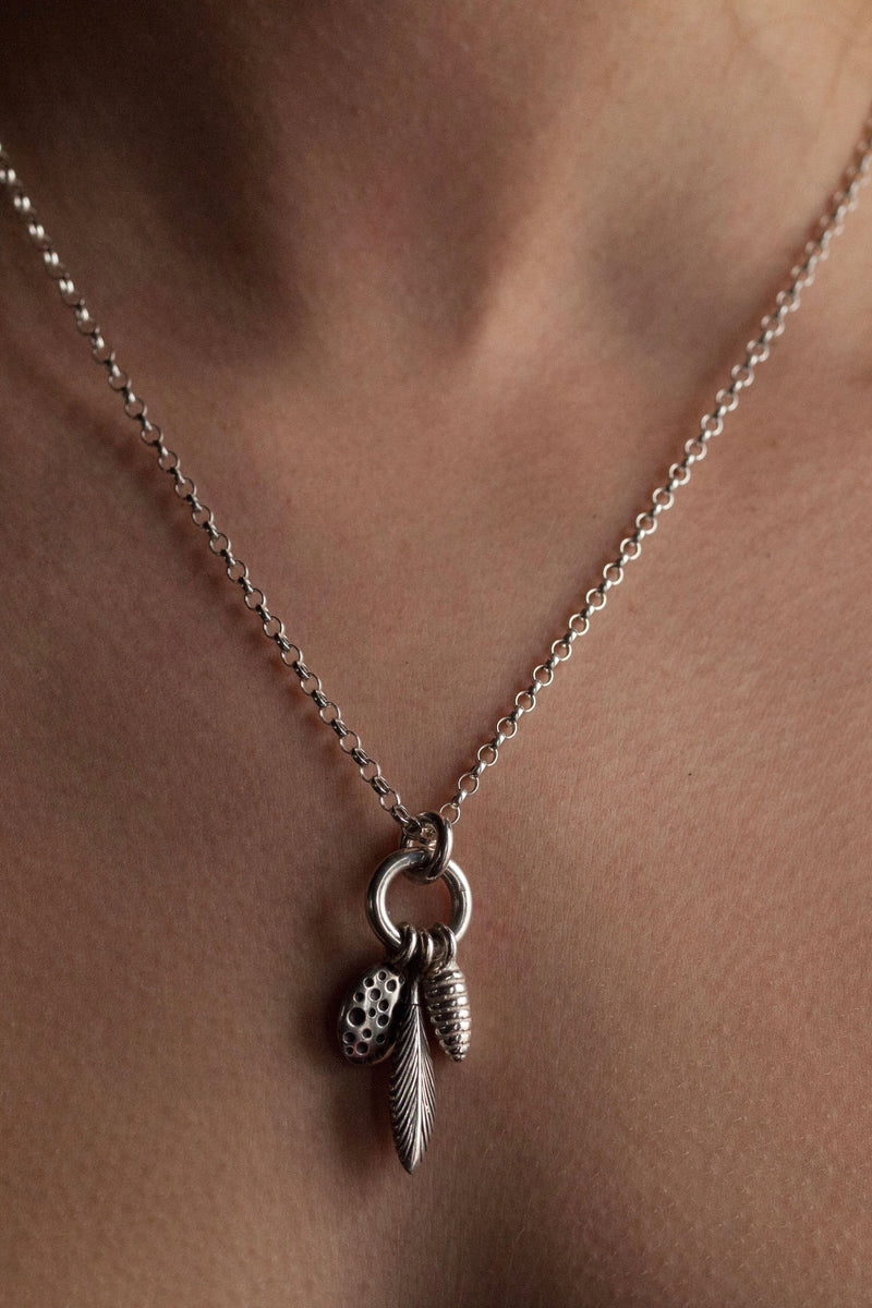 Short pendant necklace worn by model with a cluster of 3 charms inspired by seed pods and feathers