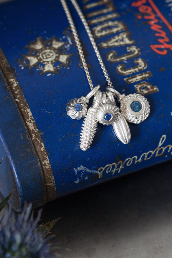 A dainty pendant featuring 5 silver pollen 3 set with a Sapphire, September's birthstone