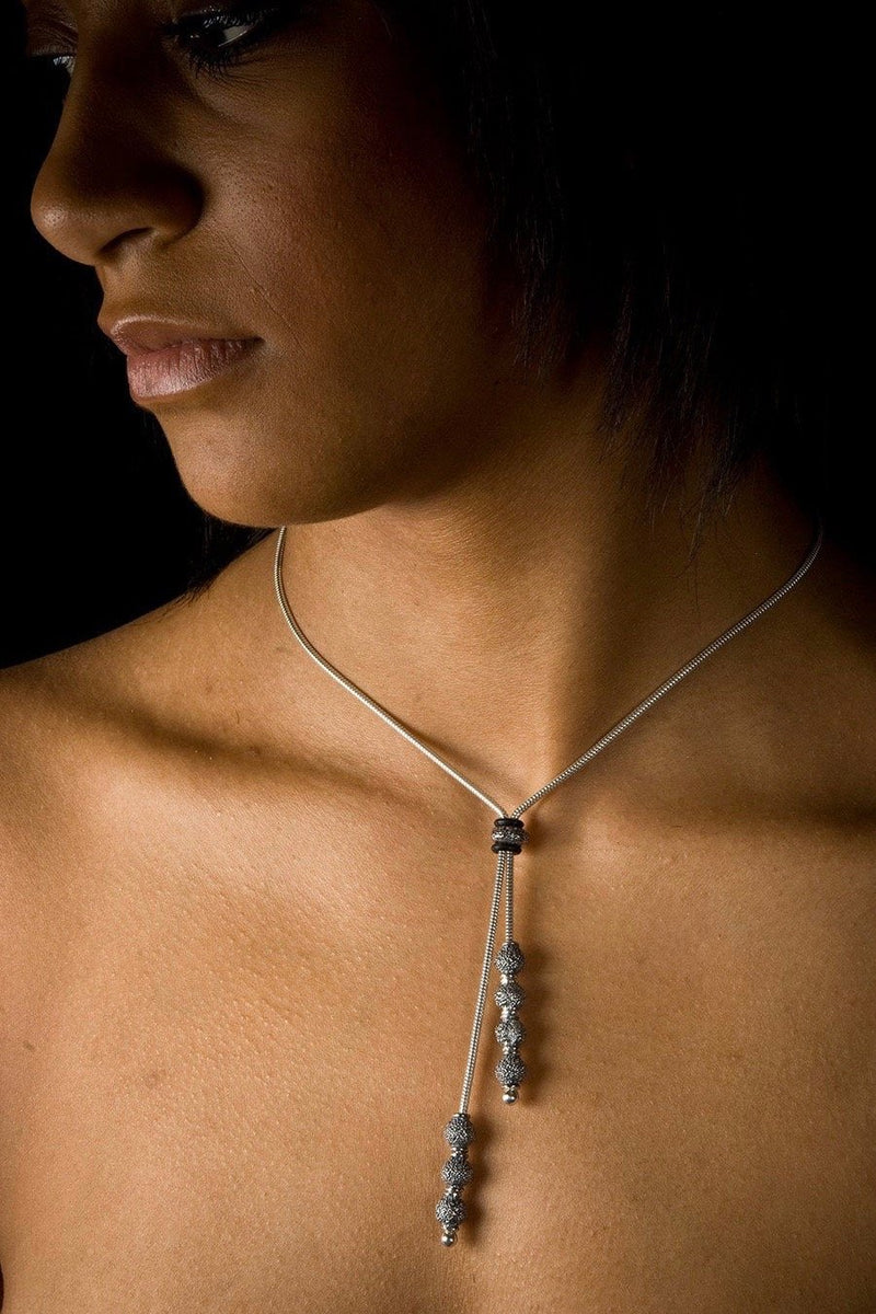 An elegant tassel pendant, worn by a model, on a snake chain threaded with seven tiny textured snow ball beads that elongates the neck