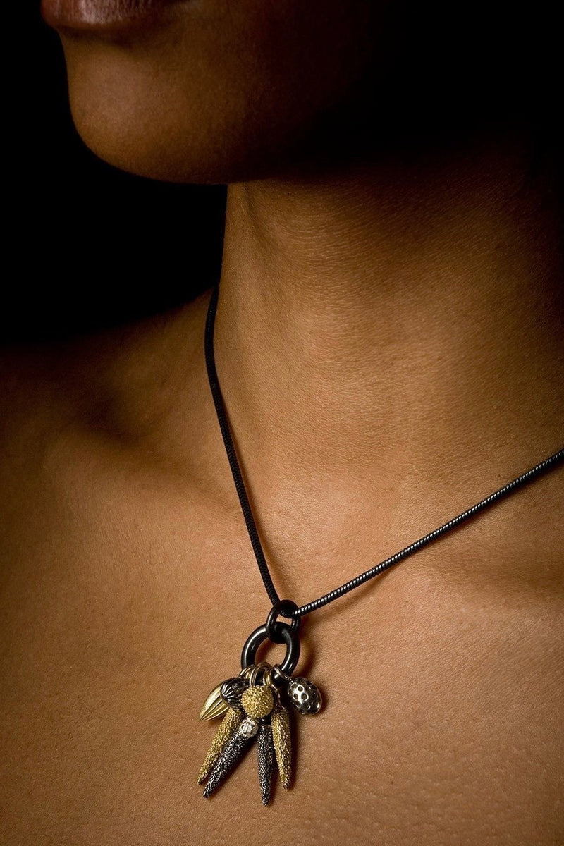 An elegant contemporary pendant necklace worn on an oxidised silver chain featuring nine charms in different metals