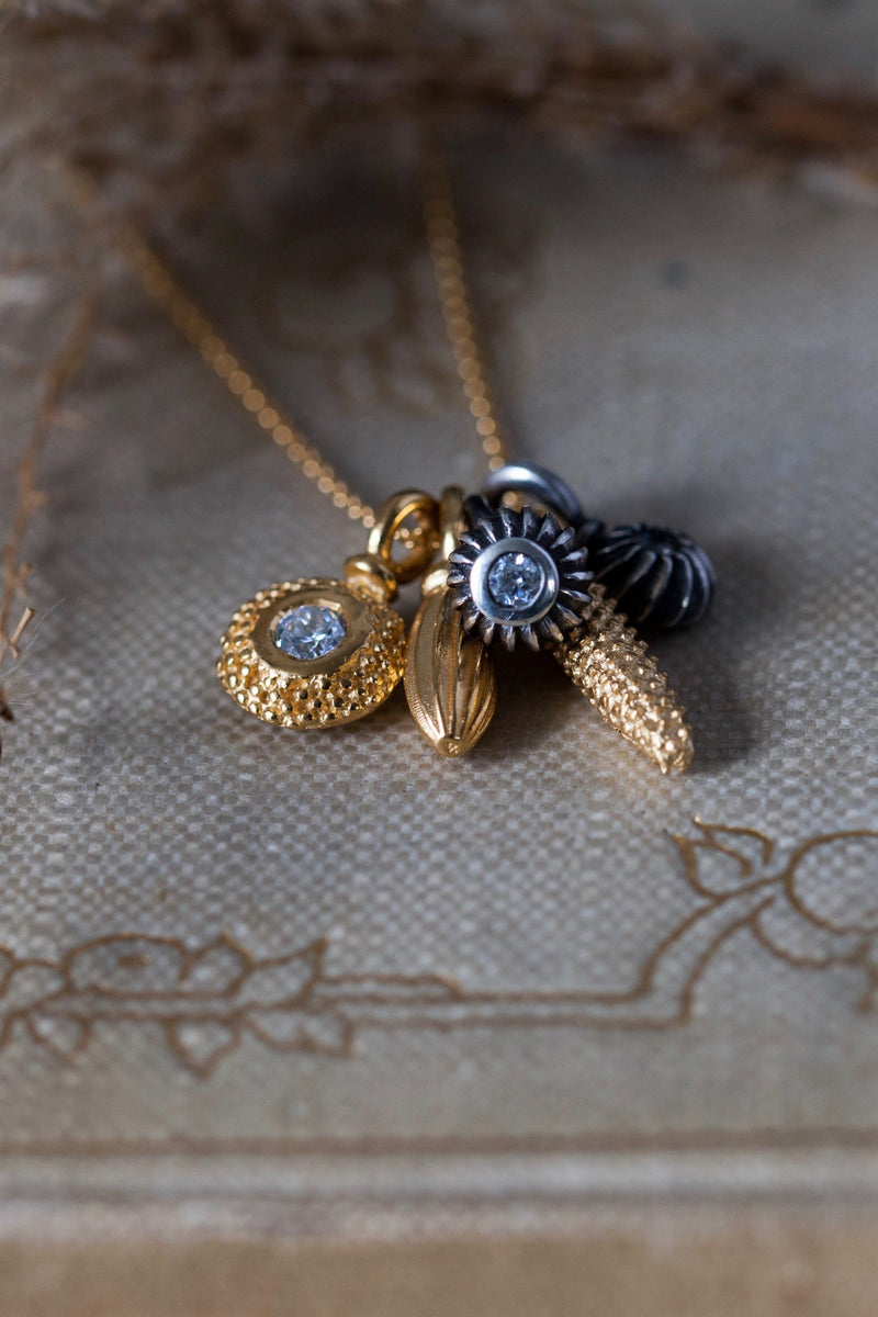 A dainty pendant featuring a cluster of five delicate gold plated silver and oxidised silver pollen charms on a fine trace gold plated silver chain, including three set with April's birthstone Cubic Zirconia.