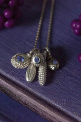 A dainty pendant featuring a cluster of five delicate silver pollen charms on a fine trace chain, including three set with December's birthstone Tanzanite.