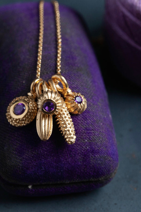 An unusual dainty pendant in yellow gold plated silver featuring a cluster of five intricate pollen charms on a fine trace chain, including three set with an Amethyst, February's birthstone.