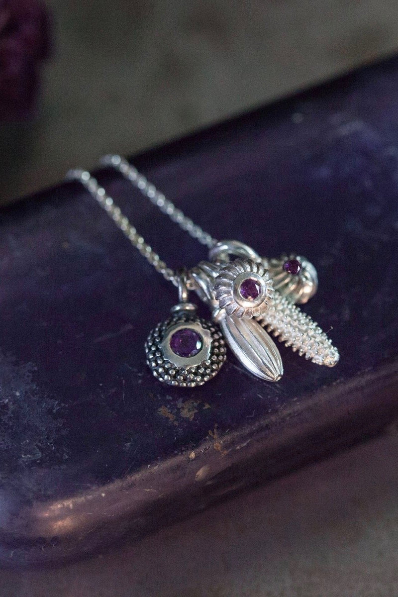 An unusual dainty pendant in silver featuring a cluster of five intricate pollen charms on a fine trace chain, including three set with an Amethyst, February's birthstone.