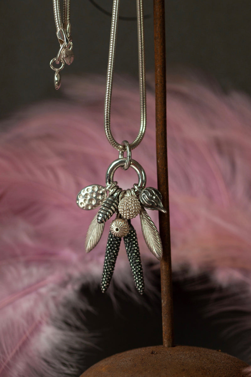 Close up of my Dream Catcher Feather and Pod Cluster Pendant necklace is hung with nine charms inspired by the shape of feathers and seed pods in silver and oxidised silver