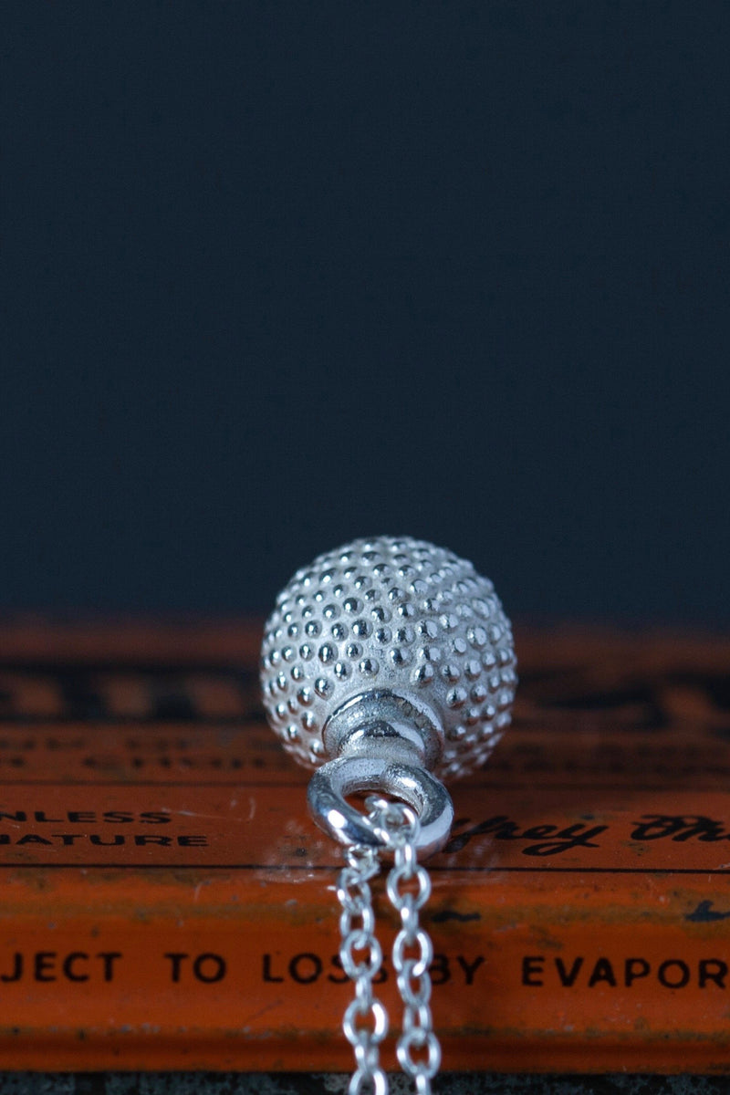 Top view of a special birthstone pendant for January – a tactile textured ball with a glistening orange Spessartite Garnet at the base