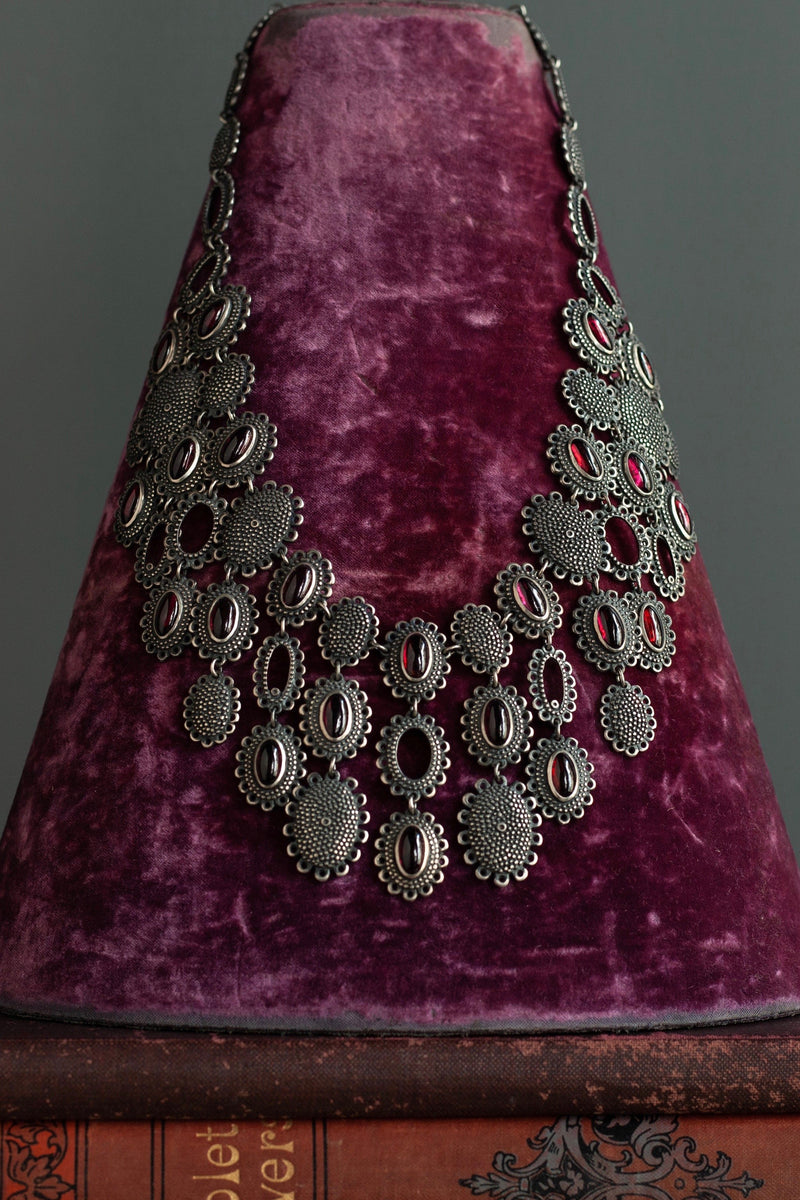 My Garnet Baroque Necklace, inspired by antique lace and ruffs, hanging on a magenta velvet jewellery stand