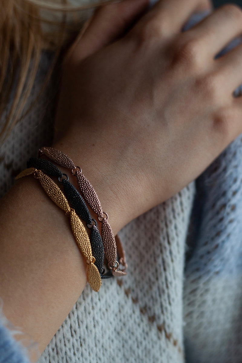 Model wearing three contrasting Petal Bracelets each with 7 textured petals linked in a chain 