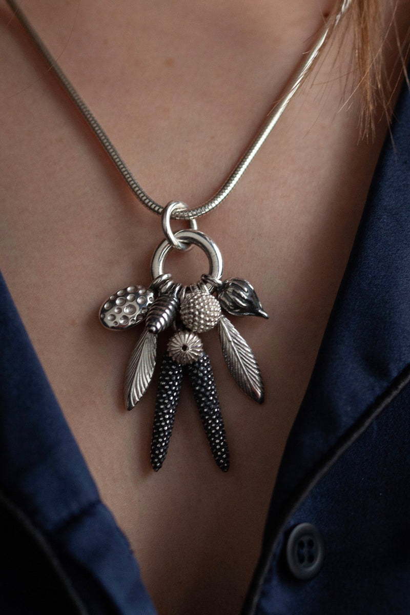My Dream Catcher Feather and Pod Cluster Pendant necklace is hung with nine charms inspired by the shape of feathers and seed pods worn by model in silver with oxidised silver and silver charms