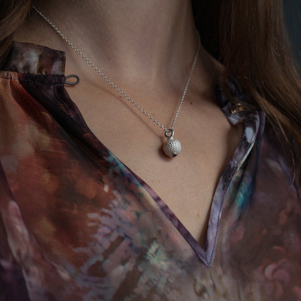 My special birthstone pendant for October in silver worn by a model – its centrepiece is a tactile textured ball with a glistening Pink Tourmaline at the base