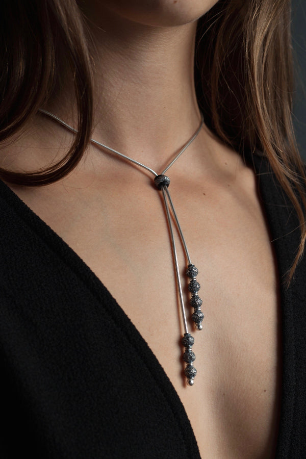 An elegant tassel pendant, worn by a model, on a snake chain threaded with seven tiny textured snow ball beads