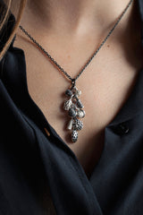 A pendant necklace worn by a model hung with a cluster of nine tiny charms in different metals inspired by seed pods