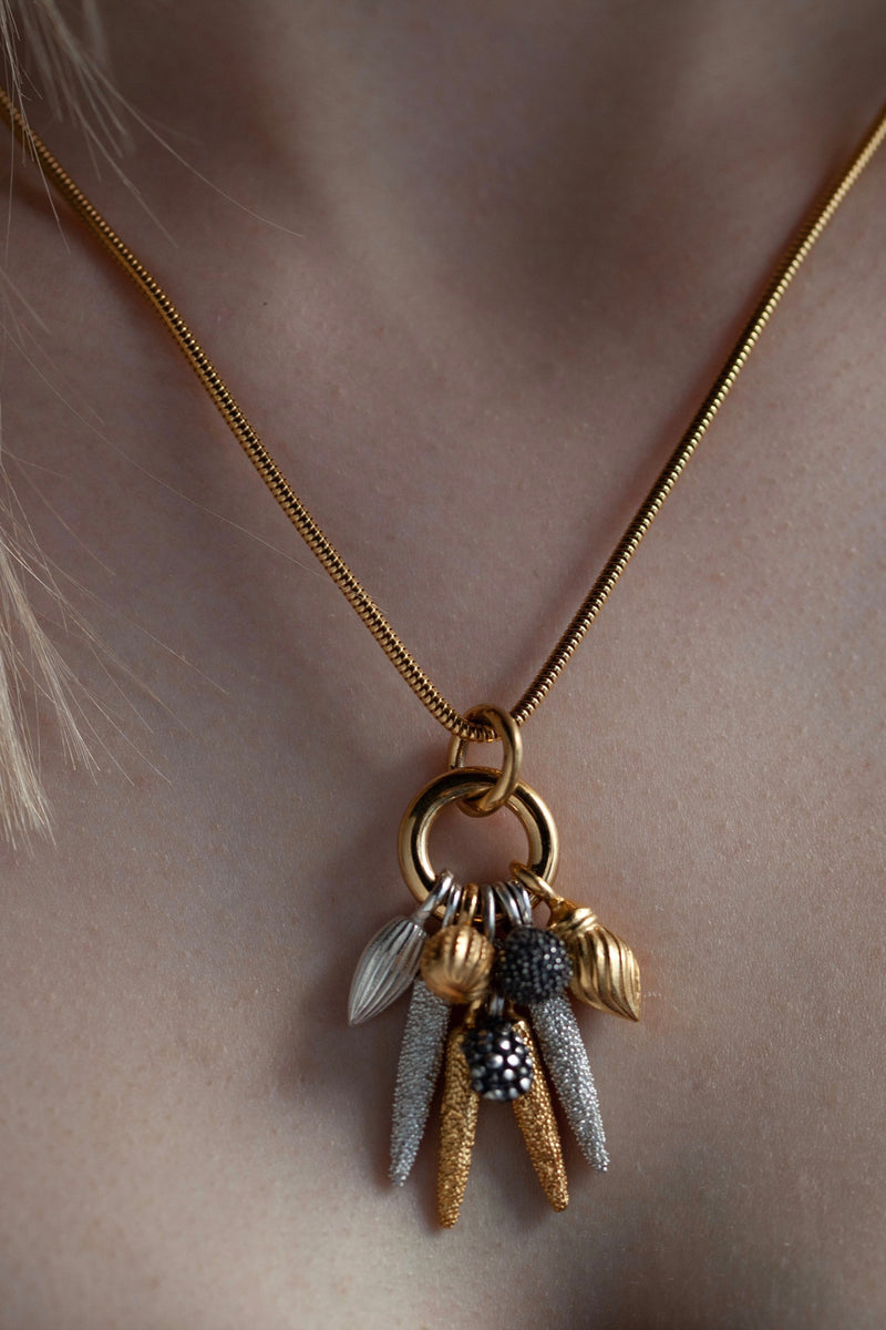 An elegant contemporary pendant necklace worn on a gold plated silver chain featuring nine charms in different metals