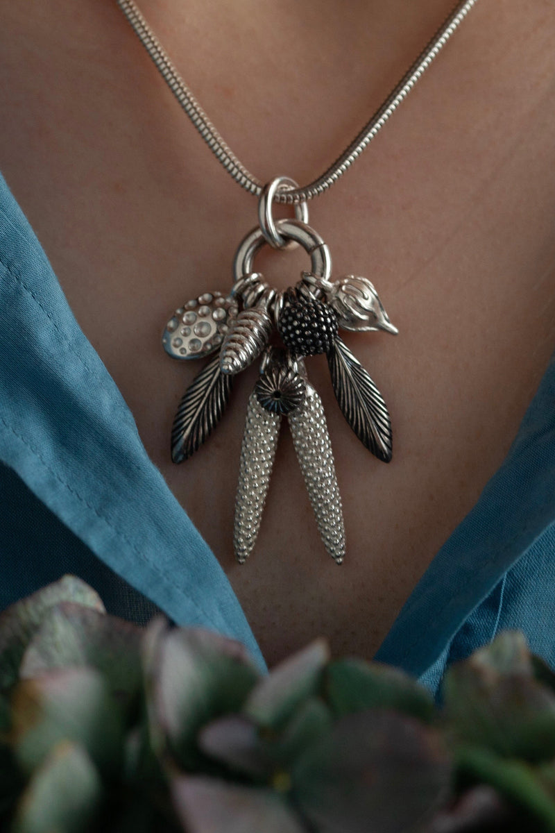 My Dream Catcher Feather and Pod Cluster Pendant necklace is hung with nine charms inspired by the shape of feathers and seed pods worn by model in silver with some oxidised silver charms