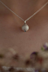 A birthstone pendant for November worn by a model – a tactile textured ball with a Swiss Blue Topaz 