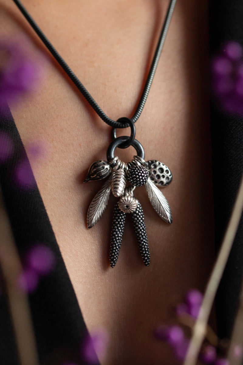 My Dream Catcher Feather and Pod Cluster Pendant necklace is hung with nine charms inspired by the shape of feathers and seed pods worn by model in oxidised silver and silver