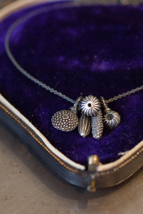 A dainty pendant featuring a cluster of five delicate textured pollen charms hanging on a fine silver trace chain displayed in a jewellery box