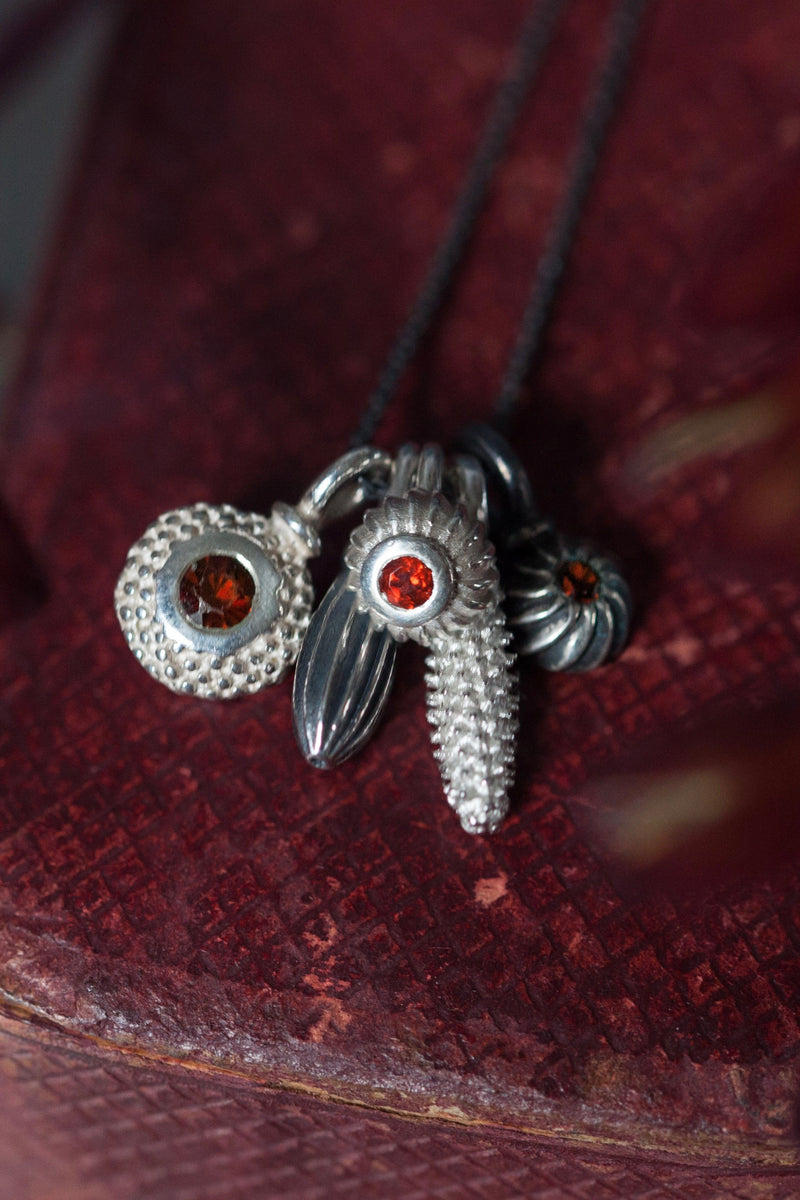 A dainty pendant featuring a cluster of five intricate silver pollen charms on a fine trace chain three set with Red Garnets January's birthstone