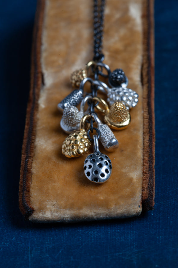 A pendant necklace hung with a cluster of nine tiny charms in different metals inspired by seed pods