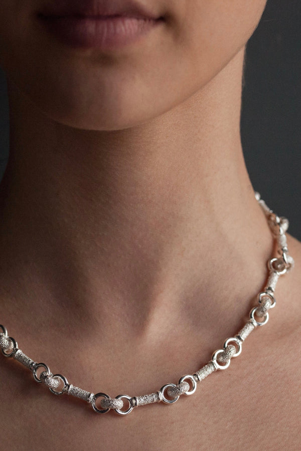A rhythmic link necklace with straight lozenges, shiny silver hoops and textured circular ‘sweeties’