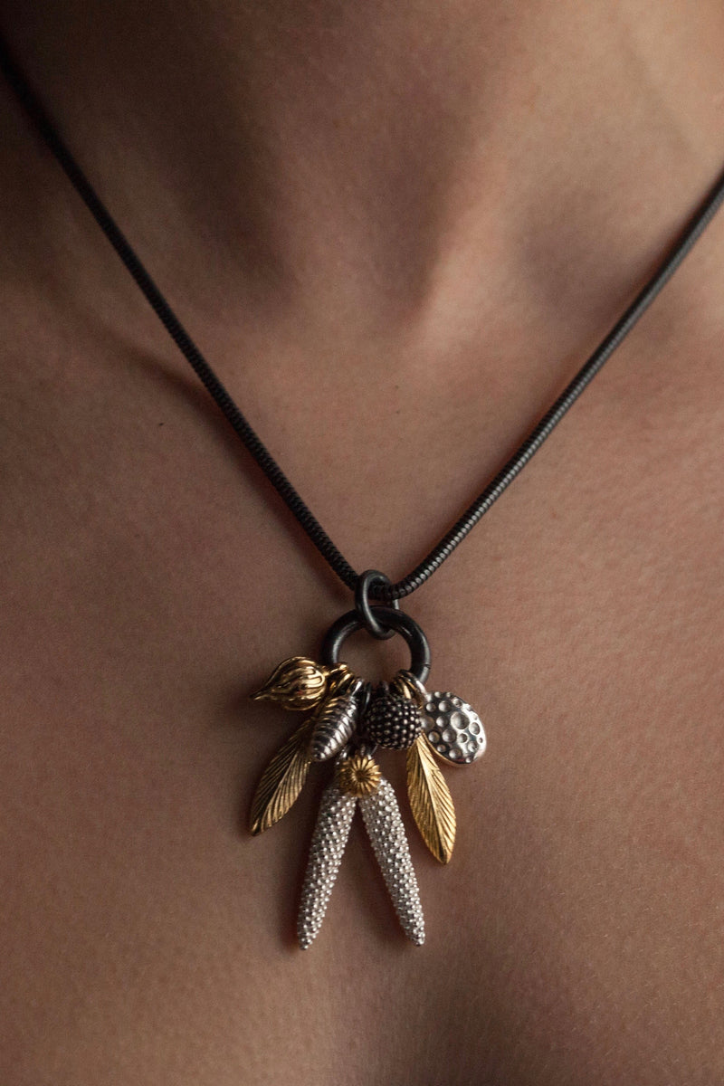 My Dream Catcher Feather and Pod Cluster Pendant necklace is hung with nine charms inspired by the shape of feathers and seed pods worn by model with a silver chain and different coloured charms 