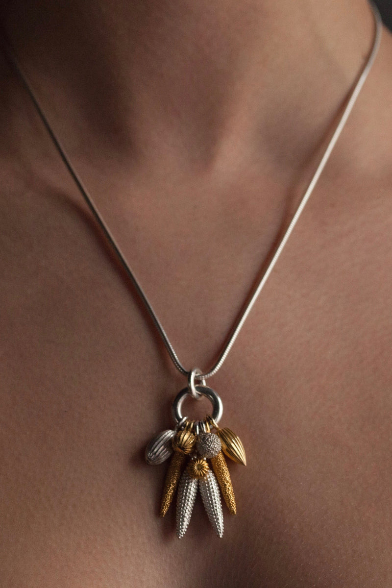 An elegant contemporary pendant necklace worn on a silver chain featuring nine charms in different metals