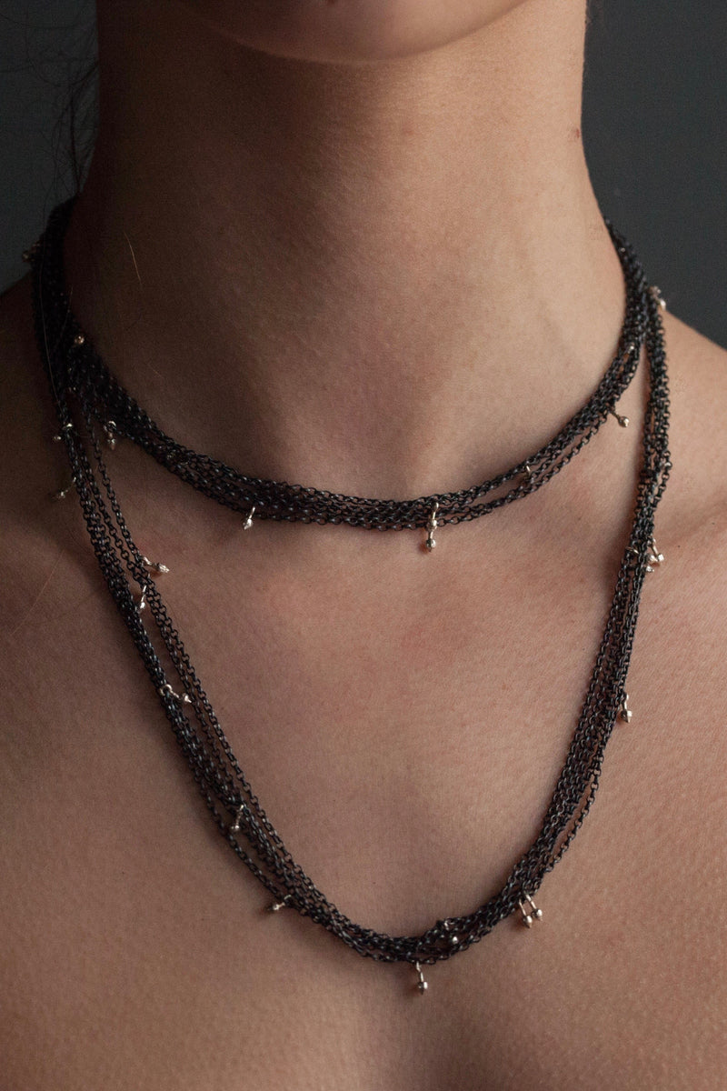 My Five Strand Trace and Pip Necklace worn double wrapped by a model comprises five delicate oxidised silver chains, decorated with miniature gold plated pips