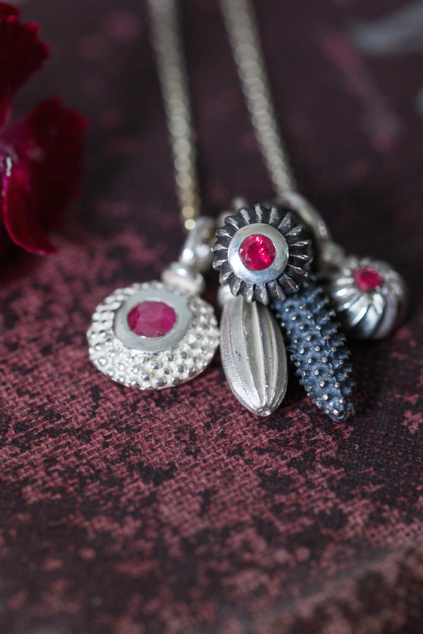 A dainty pendant featuring a cluster of 5 silver pollen charms on a fine trace chain 3 set with a Ruby July's birthstone