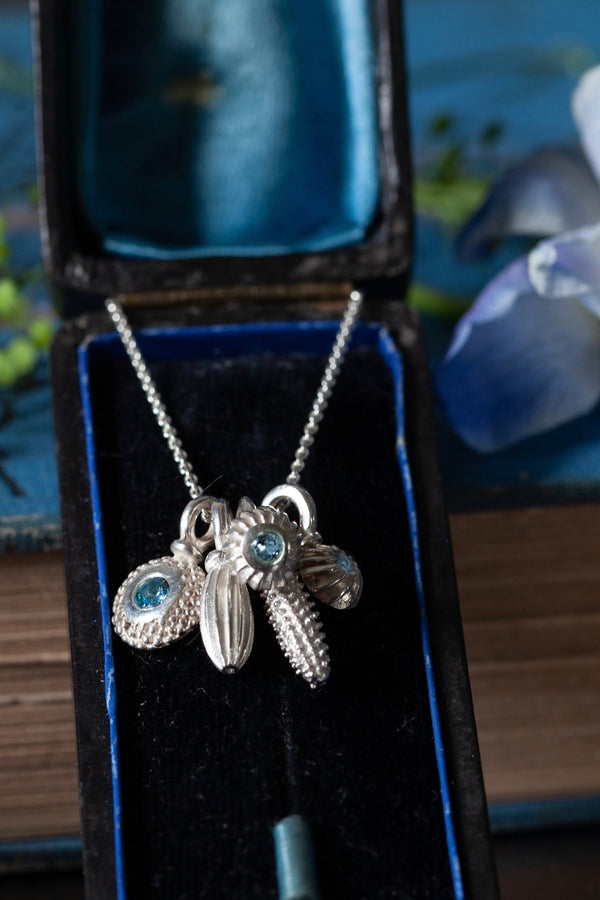 A dainty pendant featuring a cluster of 5 silver pollen charms 3 set with Aquamarine March's birthstone