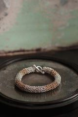 A chunky bracelet in silver and gold plated silver made from lots of daisy charms strung in a pleasing snake shape