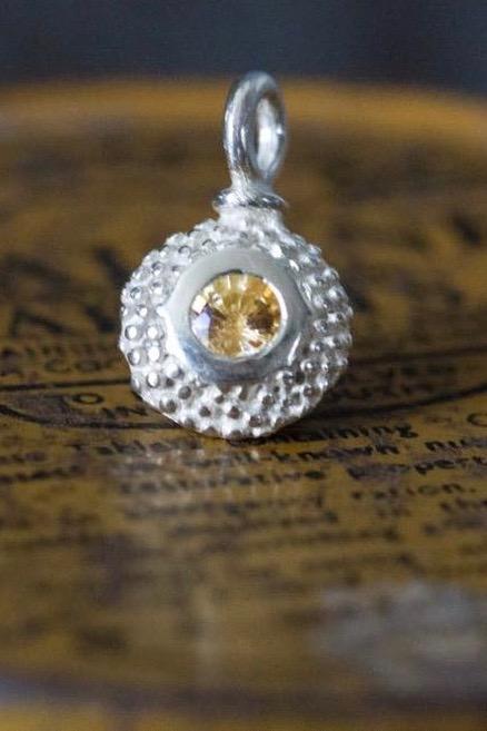 A bobbled pollen charm in silver with a glowing yellow topaz, November's birthstone.