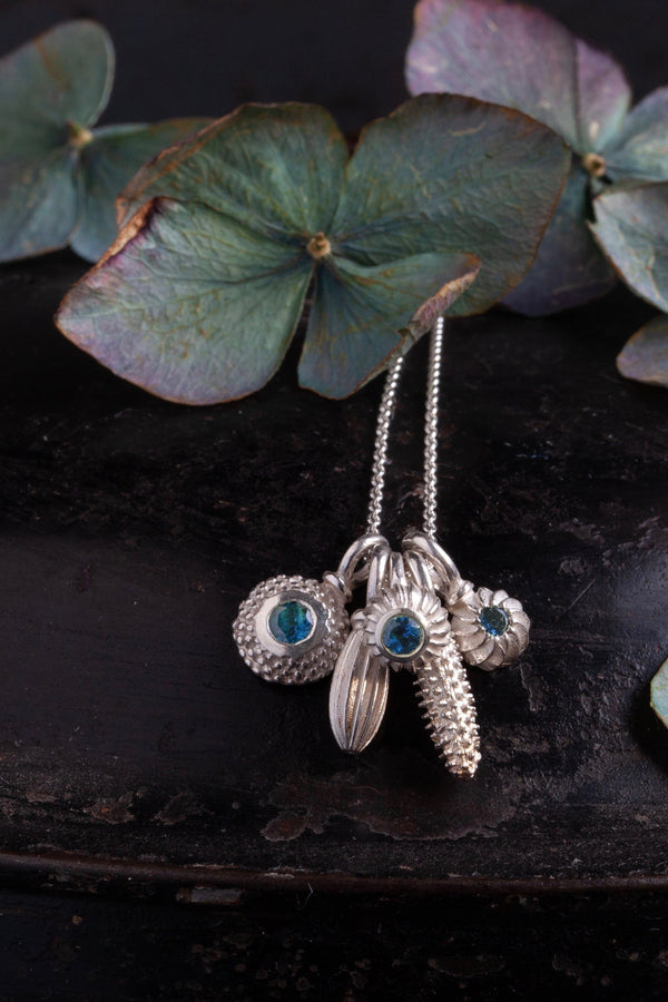 A dainty pendant with a cluster of 5 silver pollen charms 3 set with a Blue Tourmaline October's birthstone