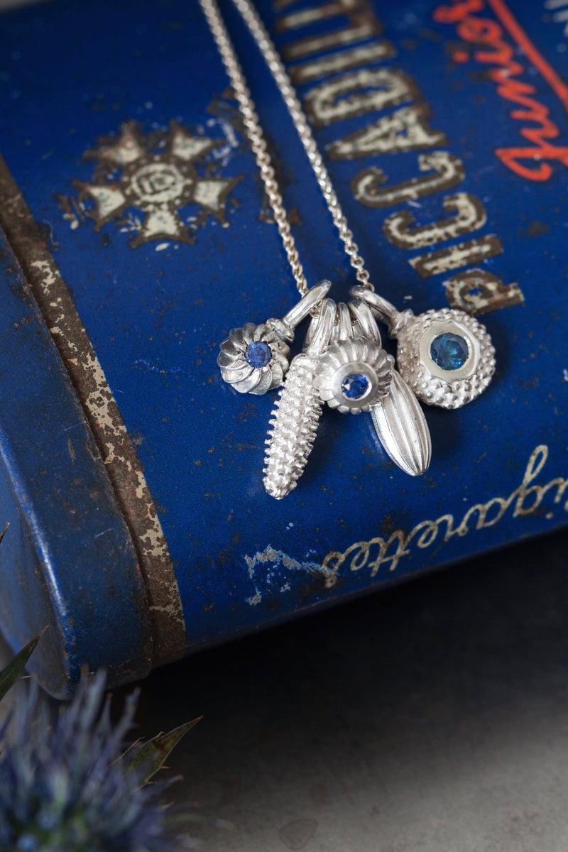 A dainty pendant featuring 5 silver pollen 3 set with a Sapphire, September's birthstone