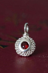 A bobbled pollen charm in silver with a ravishing red garnet, January's birthstone.