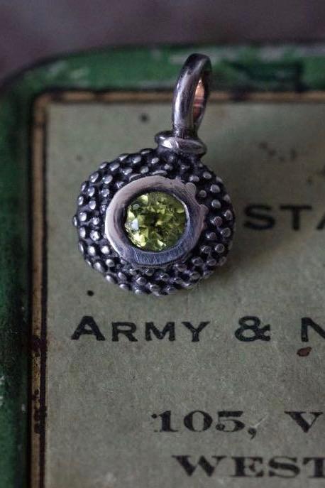 A bobbled pollen charm in oxidised silver with a glistening green peridot, August's birthstone.