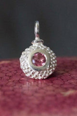 A bobbled pollen charm in silver with a mesmerising pink tourmaline, October's birthstone.